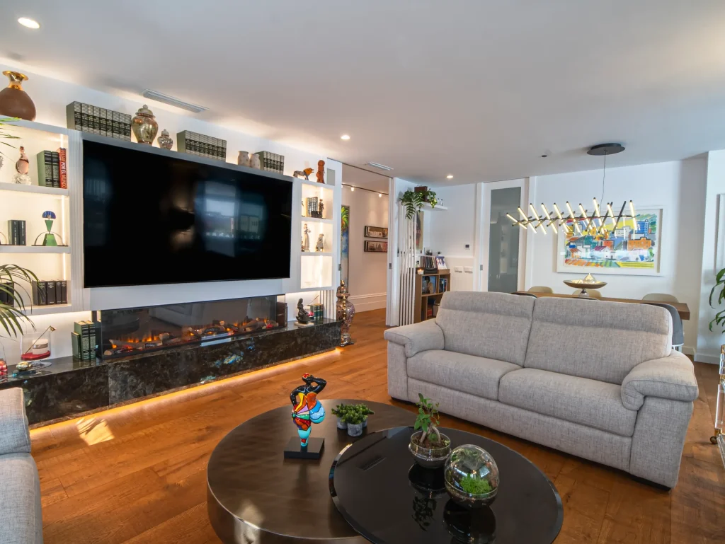 Salón con chimenea, librería iluminada y sofá gris en una vivienda de lujo en Murcia