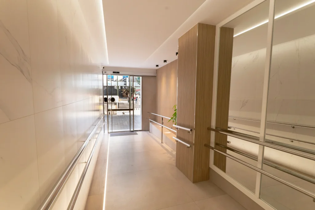 Acceso al edificio desde el hall reformado, con columnas de madera y paneles de espejo