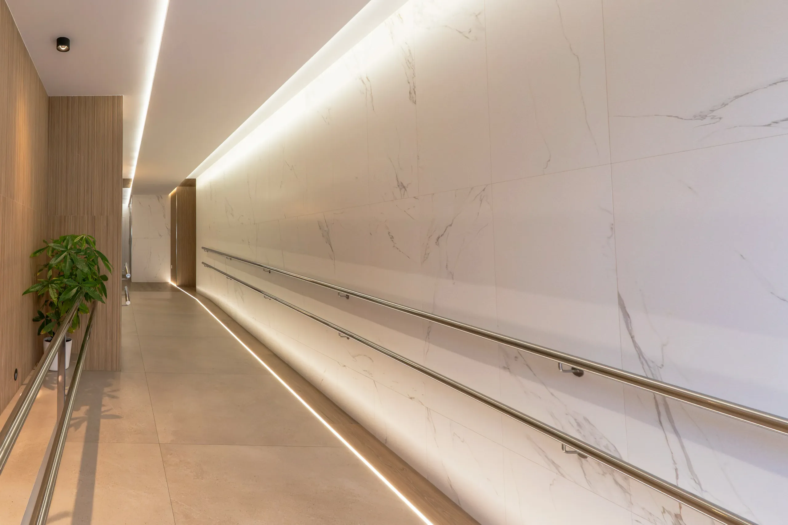 Hall de entrada reformado en el centro de Murcia, con pared de mármol y luz lineal