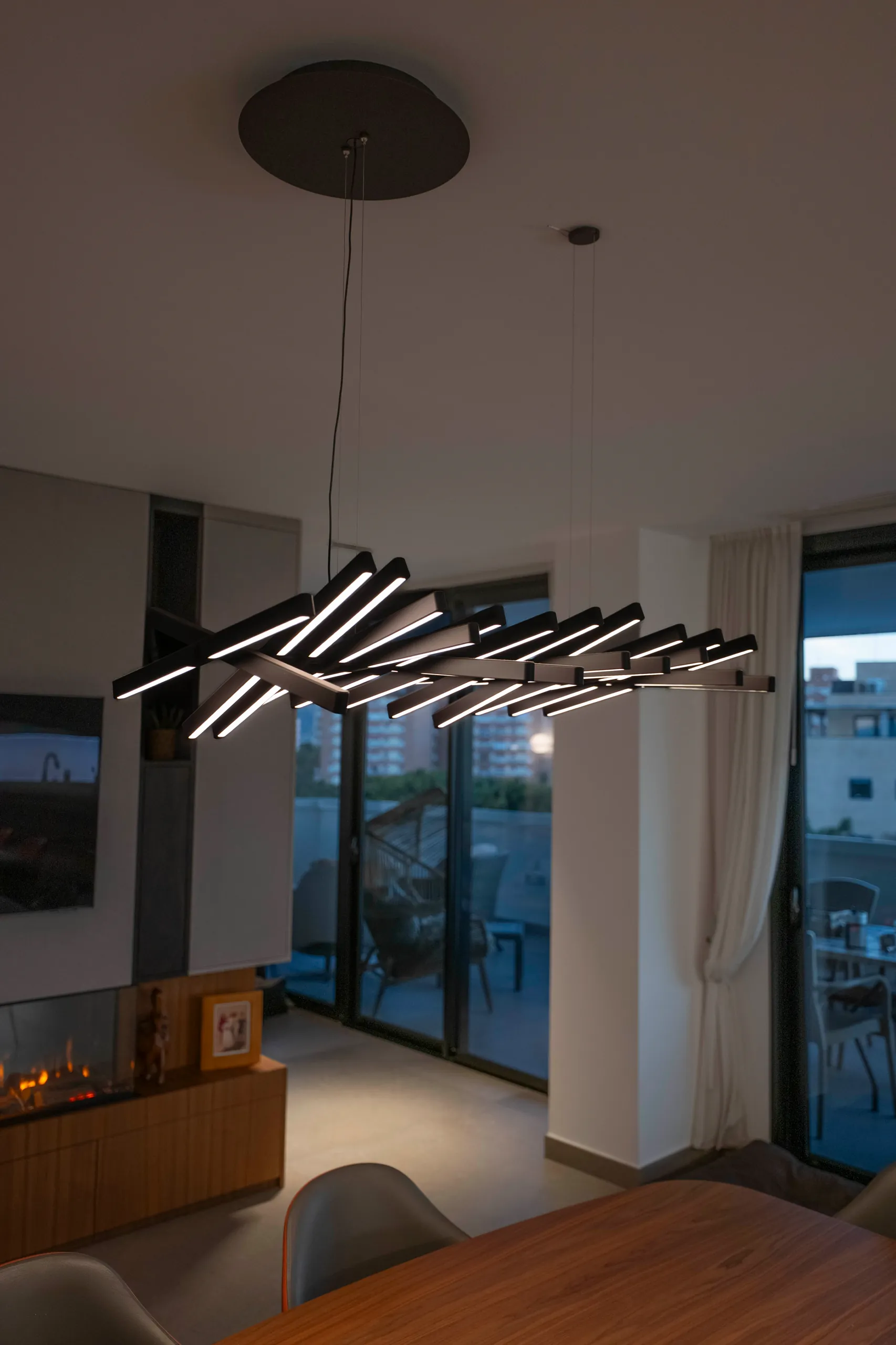Comedor con lámpara lineal suspendida y salón con ventanales al fondo