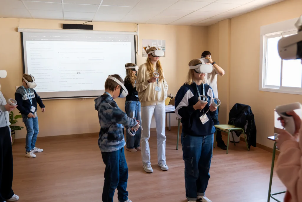 Aula con alumnos usando gafas de realidad virtual mientras un monitor les acompaña